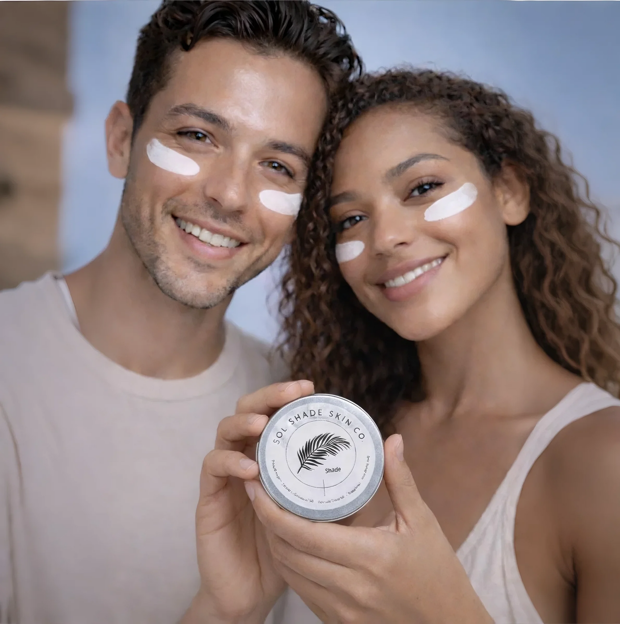 Man and woman with face cream on holding a jar, smiling at the camera.