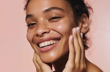 Woman with a radiant smile touching her face against a pink background